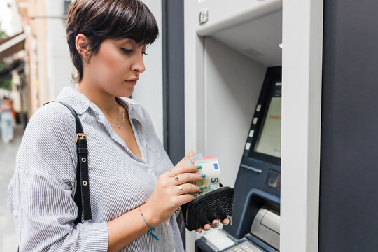 Young woman counting money from purse at ATM machine