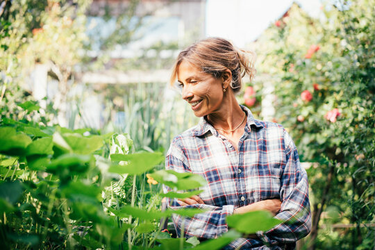 Happy mature woman with arms crossed amidst plants