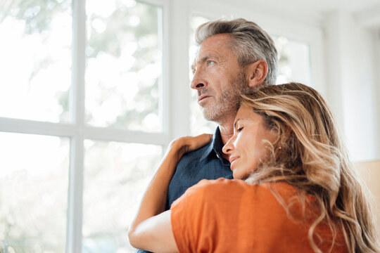 Smiling woman embracing man in front of window at home