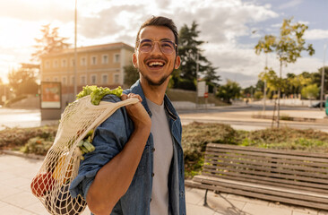 Happy young man with bag of vegetables standing at footpath