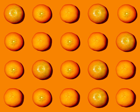 Pattern of halved tangerines flat laid against orange background