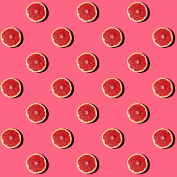 Pattern of halved grapefruits flat laid against pink background