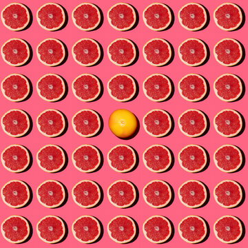 Pattern of halved grapefruits flat laid against pink background with single one lying upside down