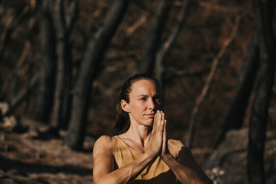 Woman standing in burnt forest praying with hands clasped