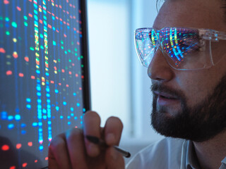 Scientist wearing protective eyeglasses analyzing DNA data on computer in laboratory