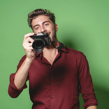 Trendy handsome guy photographer reviewing pictures from a mirrorless camera - isolated on green background