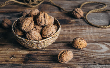 Close-up, whole walnuts in a wicker bowl on a wooden background.