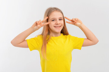 Obraz na płótnie Canvas Young beautiful teen girl with blonde hair wearing casual yellow t shirt, stands over white studio background, smiling and gesturing hands, shows victory sign
