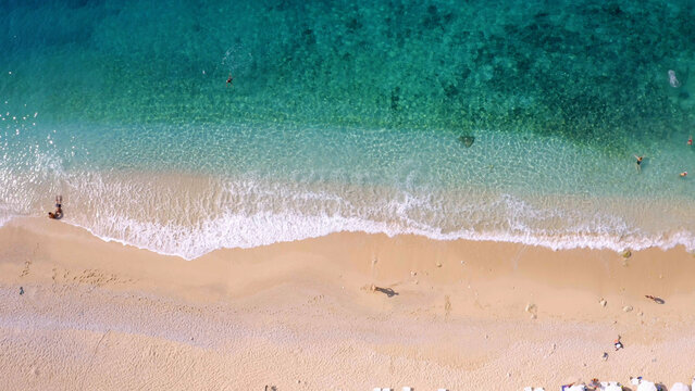 Top view people enjoying vacation on sandy beach of tropical island. Turquoise ocean waves on coastline.