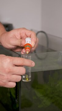 Close up of hands adding drops to test nitrite in front of freshwater aquarium. Fish tank maintenance.