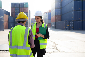 Female industrial engineer manager wears safety hardhat inspecting container cargo at warehouse storage terminal. The Inspector woman works with foreman at global import export distribution facility.
