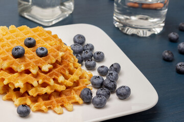 Blueberries and waffles on white plate. Glass of water and berries on the table.