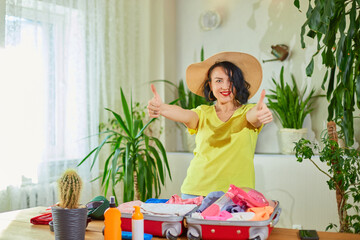 Happy woman in hat dancing, packing suitcase, getting ready for summer vacation