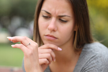 Young woman doubting looking at engagement ring