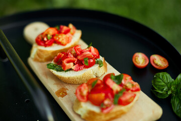 Italian bruschetta with fresh red tomatoes and basil herbs on a wooden board outdoor on the yard, backyard at home, sunlight. Classic Italy food, antipasto