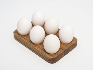 Fresh chicken eggs on rustic wooden rack isolated on white. Organic farmer products for food cooking in studio. Kitchen utensils
