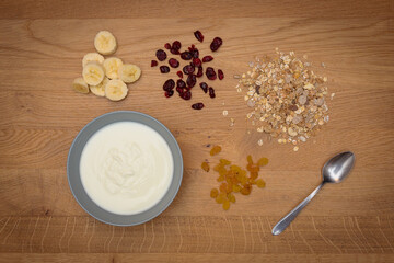 Lay flat of simple healthy breakfast with yoghurt muesli raisins cranberries and banana