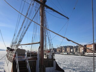 Obraz premium Aker Brygge in Oslo with a sailing ship lying in the Oslofjord with ice floes, Norway, on a beautiful cold sunny day with blue sky.