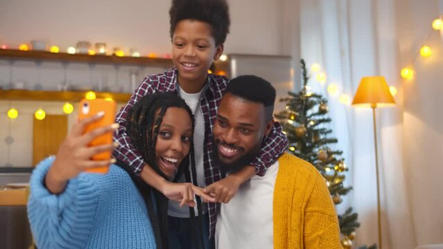 Happy African-American family taking selfie photo with smartphone in living room with decorated christmas tree