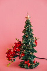 A candle in the shape of a Christmas tree with gifts with a branch of winter berries on a pink background.