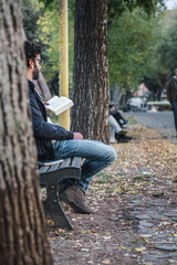 Fototapeta premium Man reading a book sitting on a bench in the park