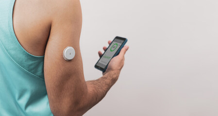 An unrecognizable man shows his defocused mobile with a continuous blood glucose test application, the patch is seen in the foreground, copy space. - obrazy, fototapety, plakaty