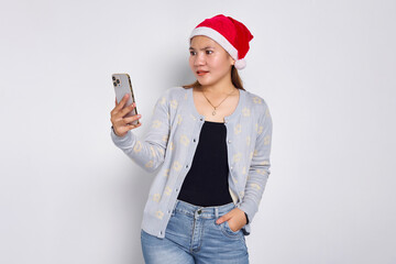 Pensive young Asian woman in a Christmas hat using mobile phone isolated over white background