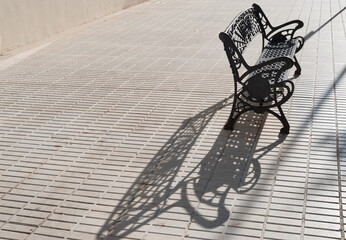 lonely black iron bench with the shadow of the sunset on the tiles