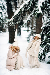 Handsome mother and daughter are having fun outdoor in winter time. Playing with snow in forest between snowy trees