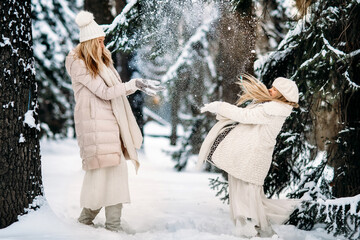 Handsome mother and daughter are having fun outdoor in winter time. Playing with snow in forest between snowy trees