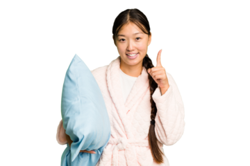 Young asian woman wearing a pajama holding a pillow isolated showing number one with finger.