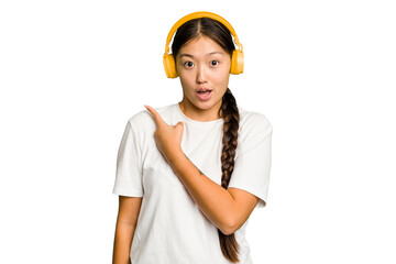 Young asian woman listening to music with headphones isolated pointing to the side