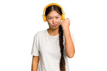 Young asian woman listening to music with headphones isolated showing fist to camera, aggressive facial expression.