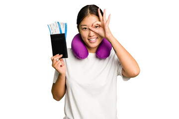 Young asian woman with inflatable travel pillow on her neck holding passport isolated excited keeping ok gesture on eye.