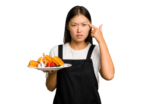 Young asian waitress woman holding waffles isolated showing a disappointment gesture with forefinger.