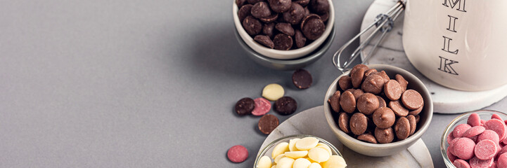 Banner with ingredients for cooking hot chocolate. White, milk, ruby and dark chocolate chips with jug milk. Over gray background. High angle view, copy space