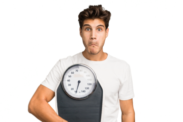 Young caucasian man holding a scale isolated shrugs shoulders and open eyes confused.