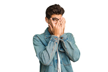 Young caucasian handsome man isolated blink at the camera through fingers, embarrassed covering face.