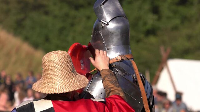 Medieval Squire Putting Shield With Belt On A Knight In Armour During Jousting Competition. medium shot