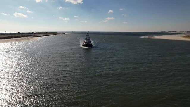 An aerial view of a tugboat on a sunny day in the East Rockaway Inlet in Queens, NY. The drone camera dolly in, truck right and pan left flying to the stern of the boat coming in from the sea.