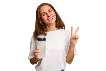 Young caucasian sport woman holding a bottle of water isolated joyful and carefree showing a peace...