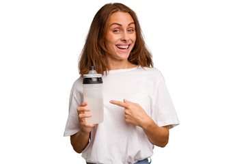 Young caucasian sport woman holding a bottle of water isolated smiling and pointing aside, showing something at blank space.