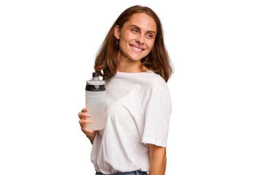 Young caucasian sport woman holding a bottle of water isolated looks aside smiling, cheerful and pleasant.