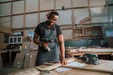 Hardworking black carpenter in factory with electric drill