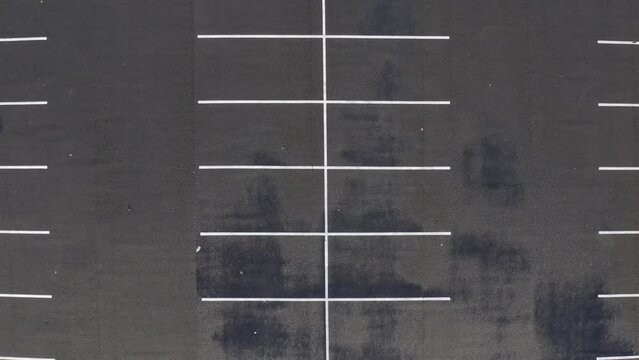 Aerial descends to white line design painted on dark paved parking lot