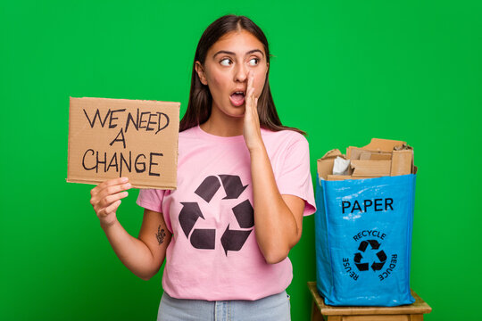 Young caucasian recycler woman holding a we need a change placard isolated is saying a secret hot braking news and looking aside