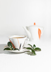A branch and leaves of Yaupon holly lie near a porcelain cup and teapot on a table. Tonic herbal tea.