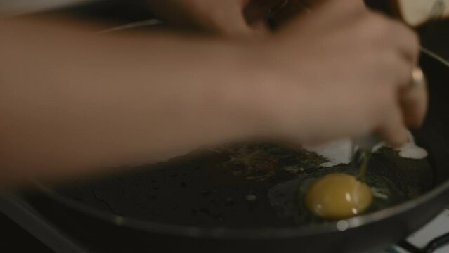Hand cracking an egg into Teflon frying pan on a gas cook stove