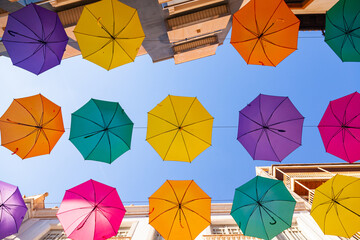 Multi-colored umbrellas hang on the street along the houses against the sky.