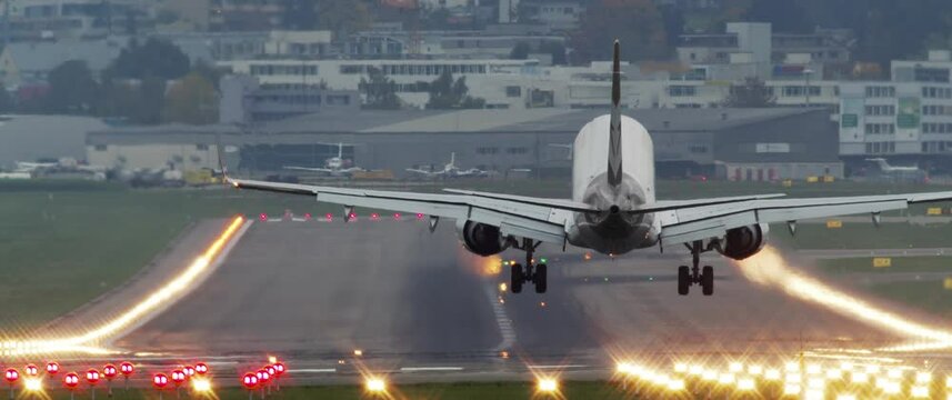 Long shot of passenger airplane flying low over the runway lights and lands at the airport. Zurich, Switzerland
